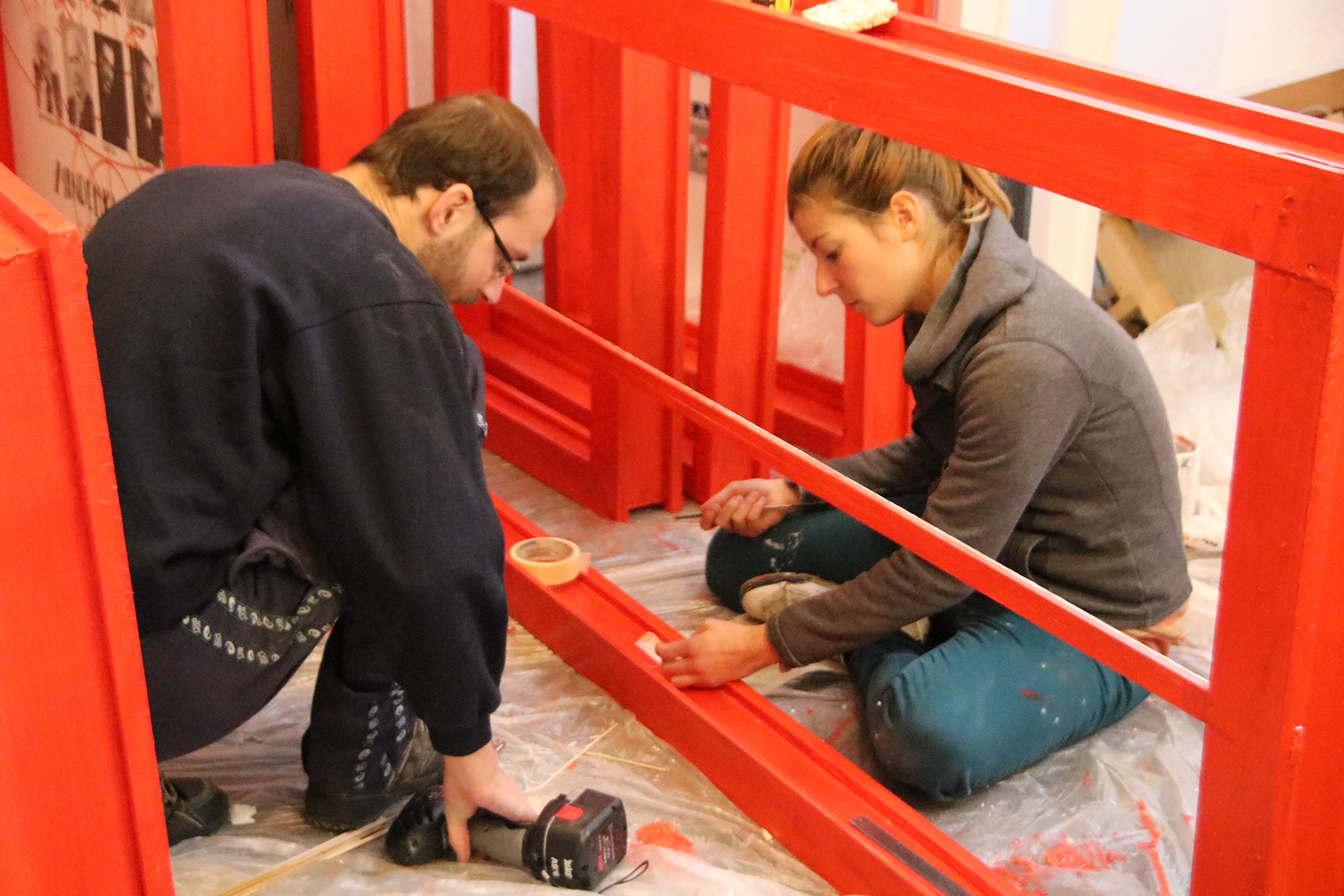 people painting a door frame with red cover paint